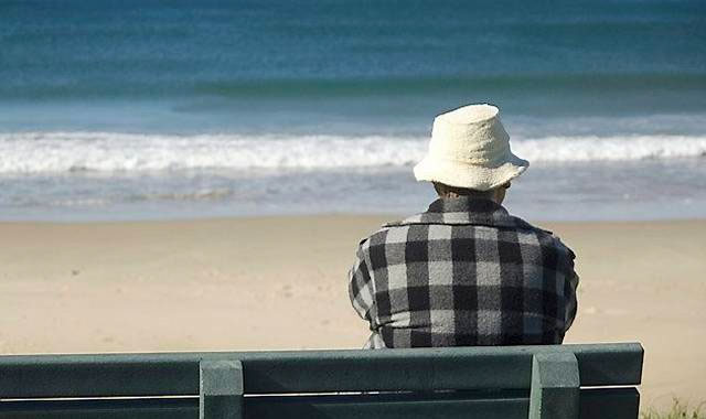 Ældre mand med skovmandsskjorte jakke og hat sidder ved stranden